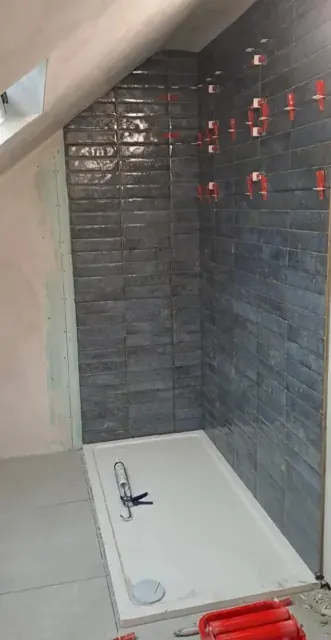 Charcoal subway shower wall tiles under sloped ceiling and white shower tray, with leveling clips