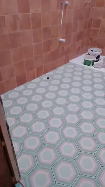 Patterned hexagonal bathroom floor tiles beside pink tiled wall and pipe stubs