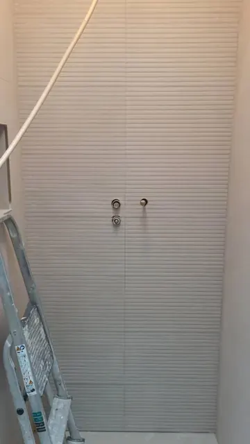 Ribbed white shower wall with mixer pipe stubs and ladder