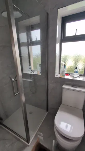 Grey-tiled bathroom with a glass shower enclosure, rainfall shower and toilet